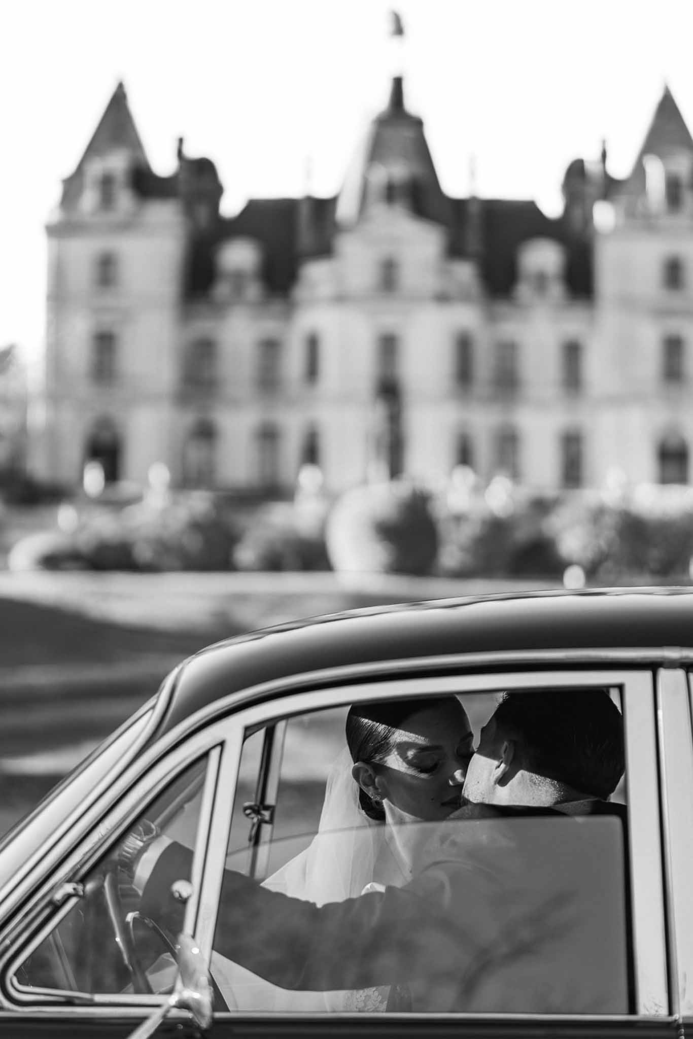 Couple kissing inside vintage car with Chateau du Terral in background