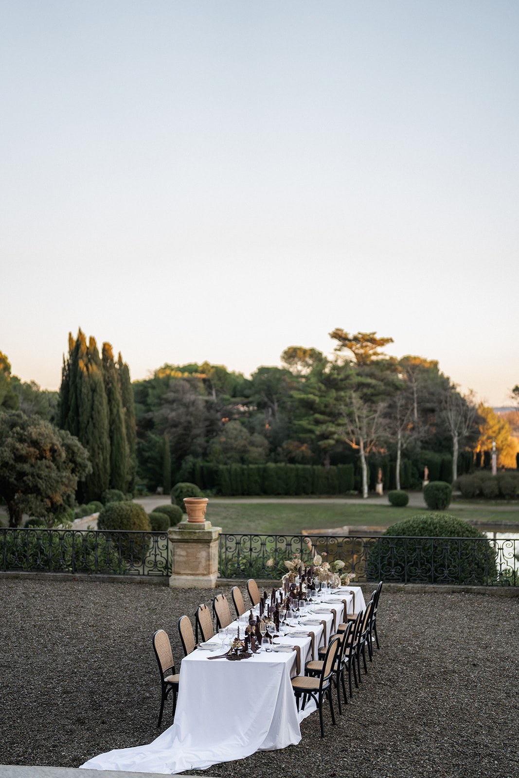 Wide reception table on chateau terrace at dusk overlooking formal garden at Chateau du Terral