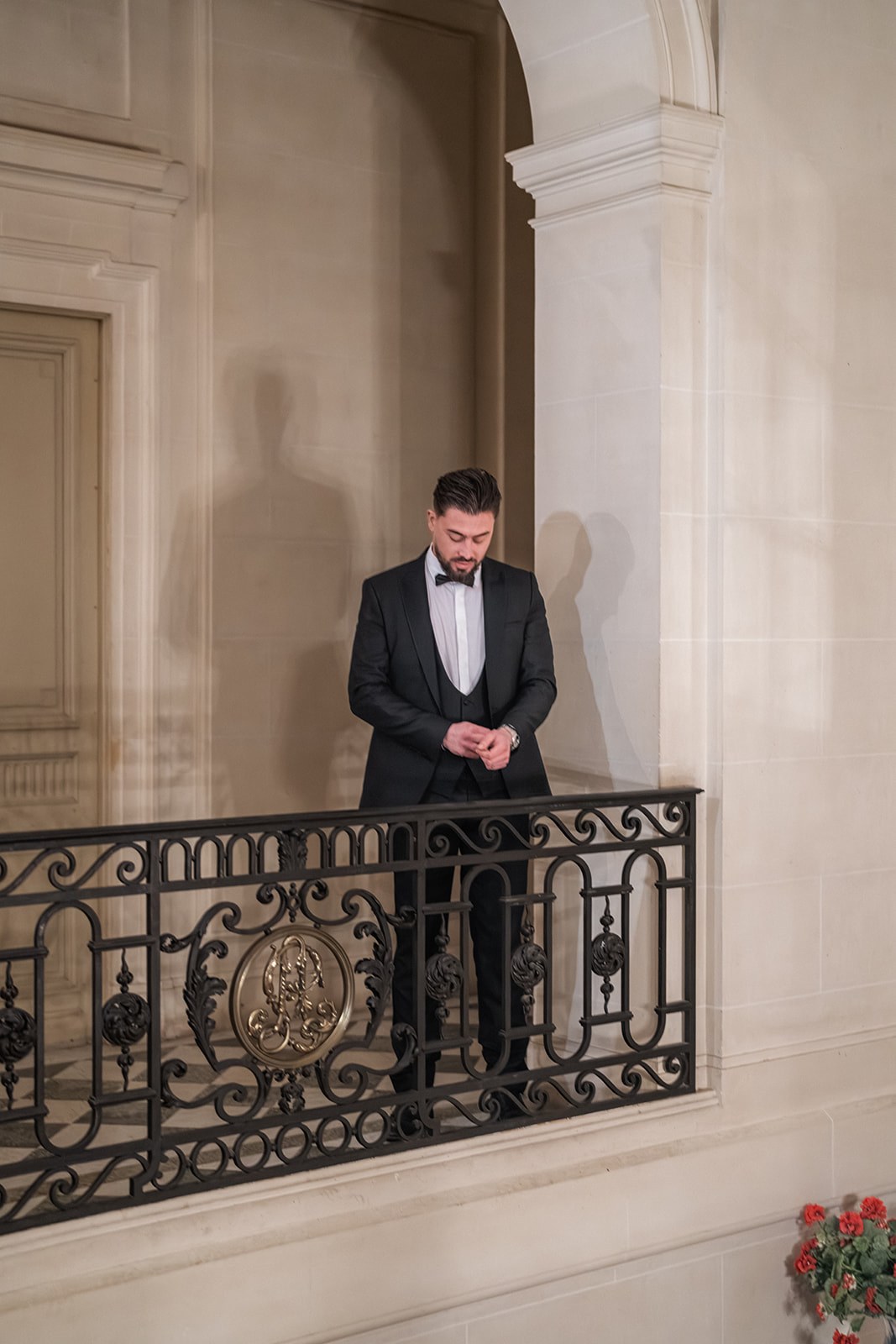 Groom in black tuxedo and bow tie adjusting cuff on chateau balcony at Chateau du Terral
