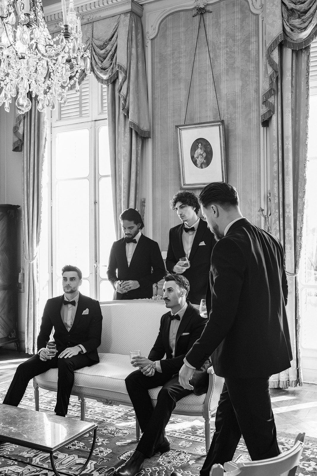 Black and white groomsmen in tuxedos relaxing in chateau salon at Chateau du Terral
