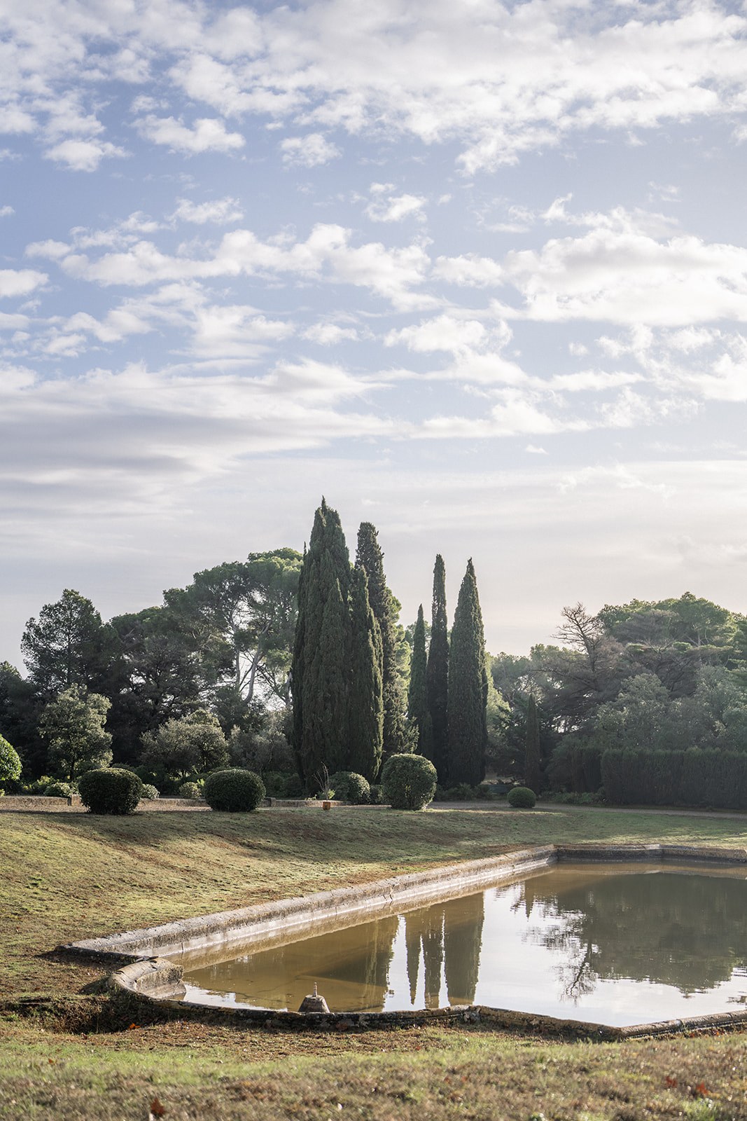 Tall cypress trees reflected in chateau pond at golden hour at Chateau du Terral