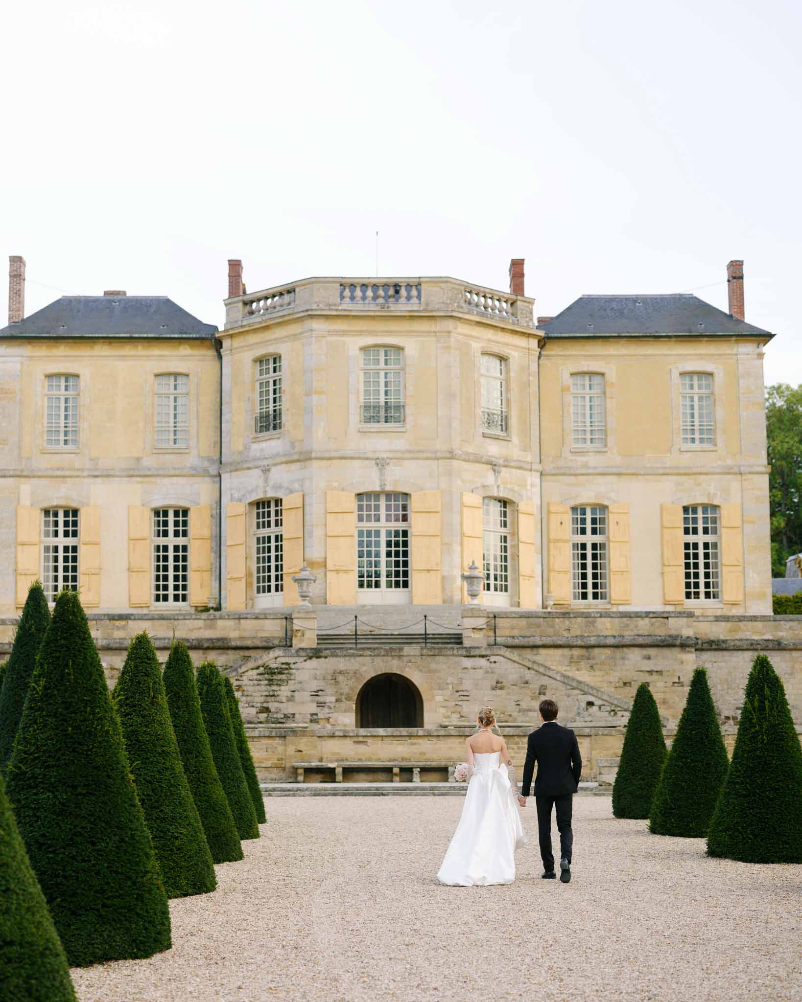 Couple walking hand in hand towards Chateau de Villette, photographed from behind