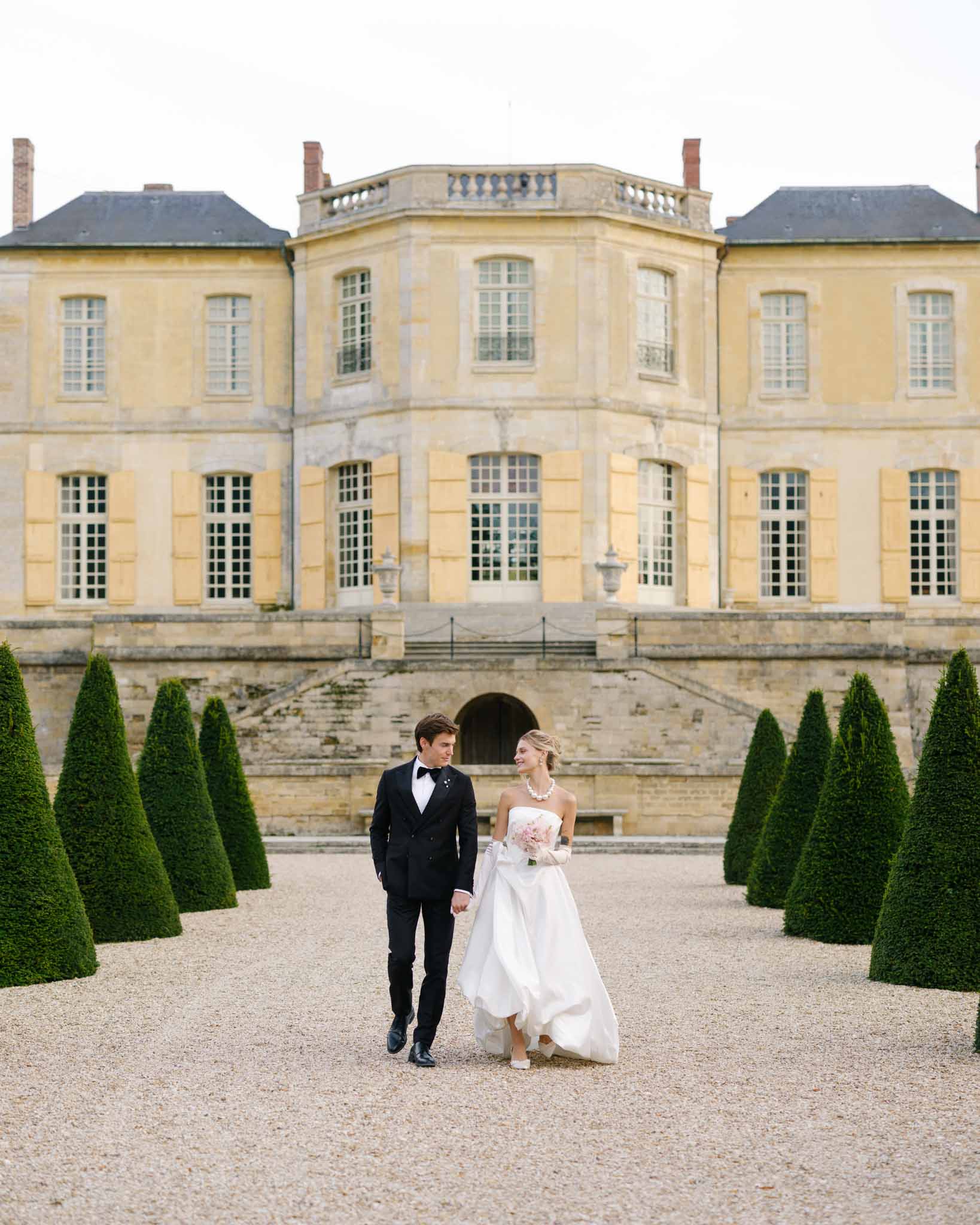 Couple walking through formal gardens with chateau in background