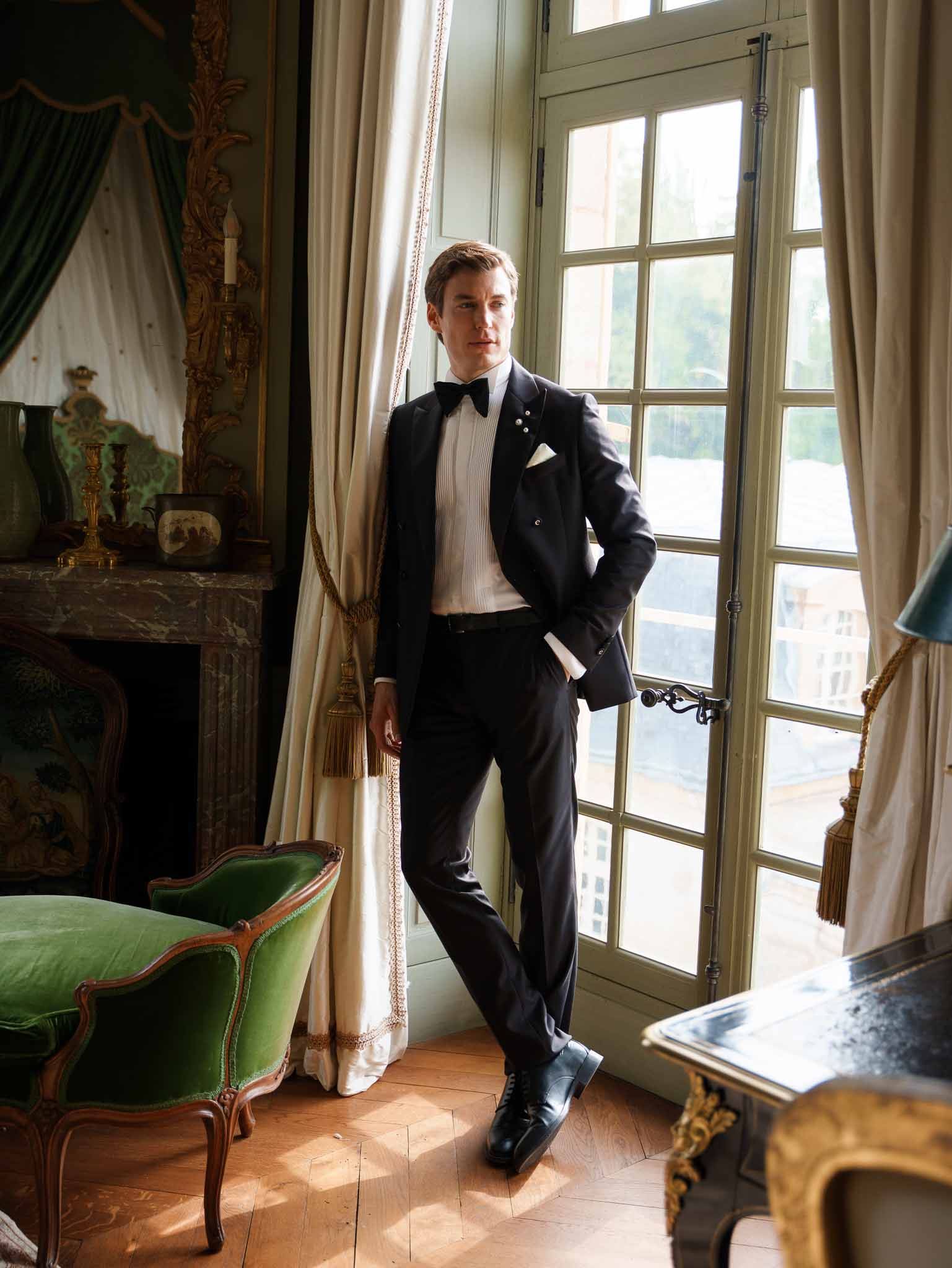 Groom standing in silhouette by a tall window at the chateau