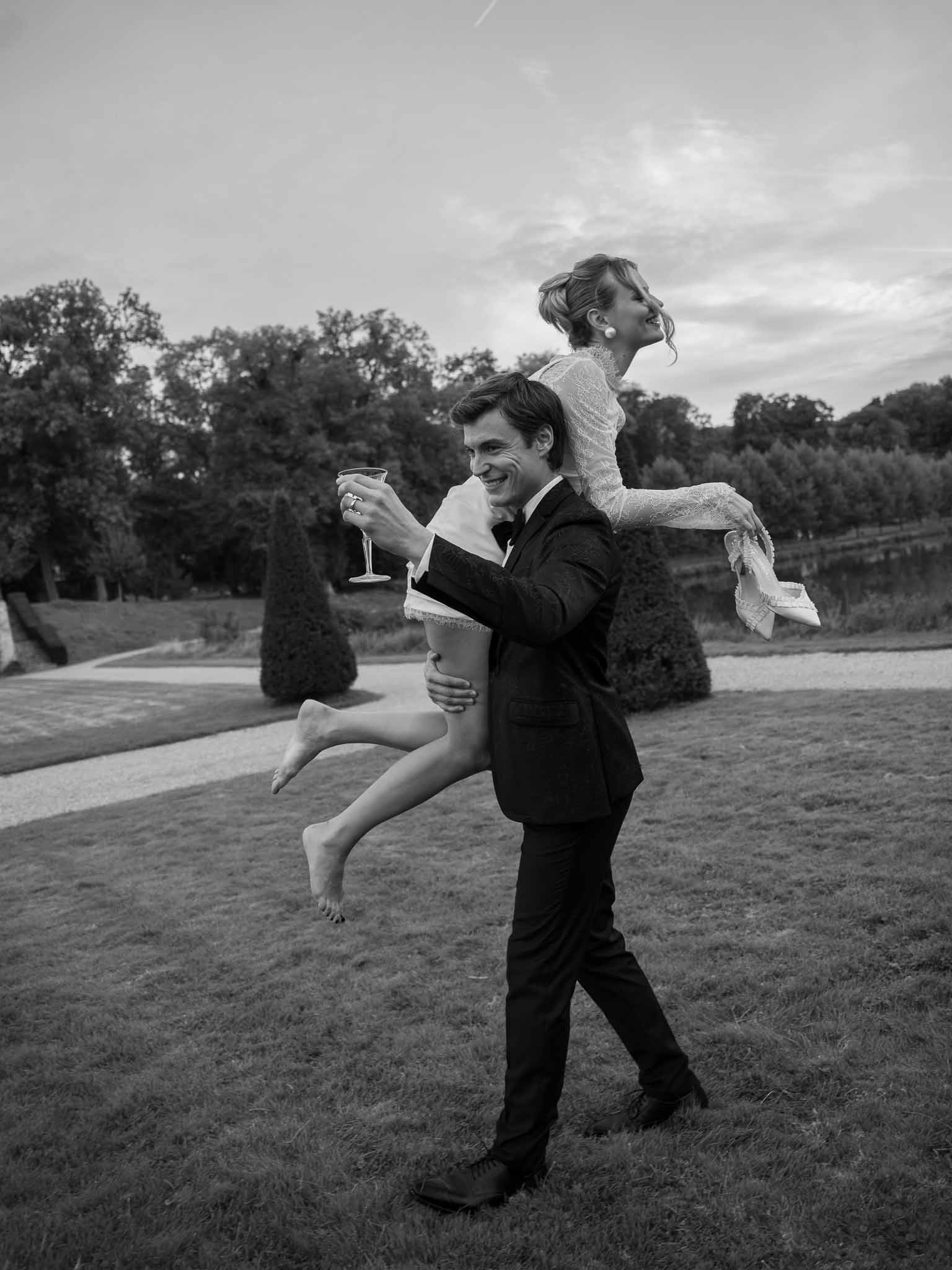 Groom lifting bride who holds a champagne glass at the reception